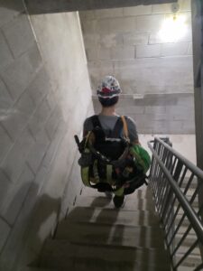 드라이월 현장 작업 사진 — 계단에서 장비 메고 있는 모습